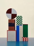 HAY Tin Container, Large, Off-White and Red, lidded tinplate storage tin, stacked with striped and checkerboard tins and a round lid on a blue plinth