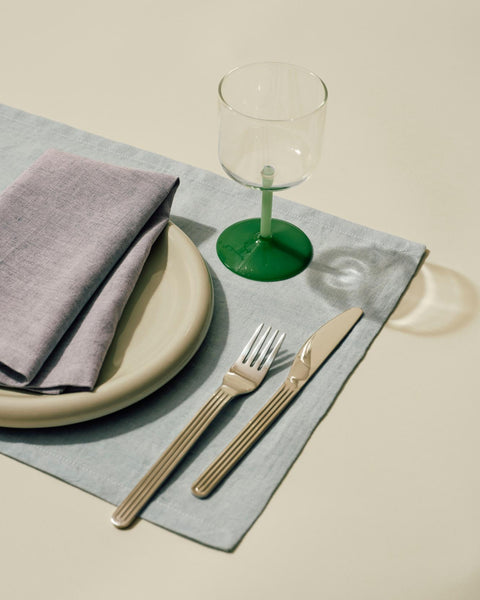 HAY Tint Wine Glasses, Jade Light and Dark Green, tinted borosilicate wine glasses, one glass at a place setting with a blue mat, plates, cutlery