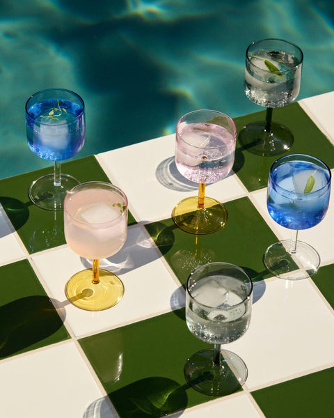 HAY Tint Wine Glasses, Blue, tinted borosilicate wine glasses, filled drinks on green and cream checkerboard tiles beside a swimming pool