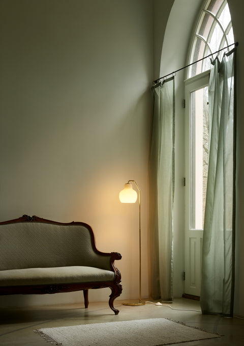 Louis Poulsen VL Ring Crown floor lamp with brass base and opal glass shade next to a vintage sofa, minimalist Danish design living room