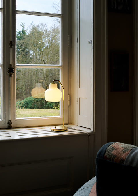 Scandinavian brass table lamp with opal glass by Louis Poulsen VL Ring Crown glowing on a window ledge in a cozy living room.