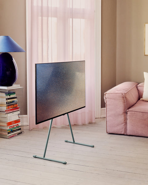 Pedestal Viva TV Stand in Charcoal, steel TV floor stand, holding a screen in a living room with a pink sofa and curtains