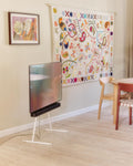 Pedestal Viva TV Stand in Pearl, steel TV floor stand, holding a screen in a child's room with patterned wallpaper