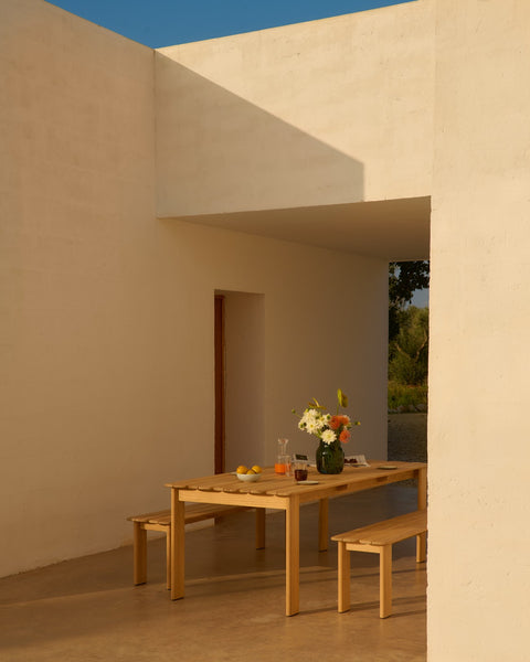 Muuto Assemble teak outdoor dining table with matching benches on covered patio