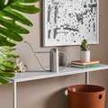Li'l Dripdrop Watering Can by Blu Dot in polished stainless steel, styled on a marble console table with plants and books