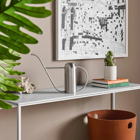 Li'l Dripdrop Watering Can by Blu Dot in polished stainless steel, styled on a marble console table with plants and books