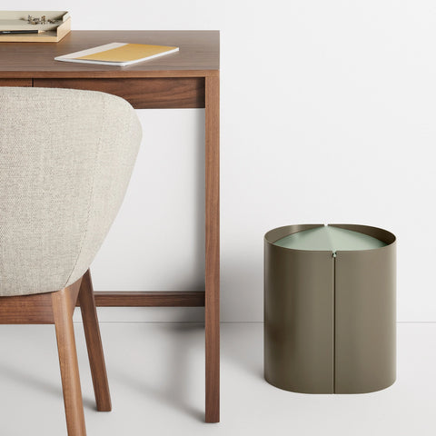 Blu Dot Binwell Wastebasket in Dark Olive with sage swing-top lid styled next to a walnut desk