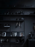 String Furniture black shelving system styled with kitchenware, books, and utensils in a dark interior