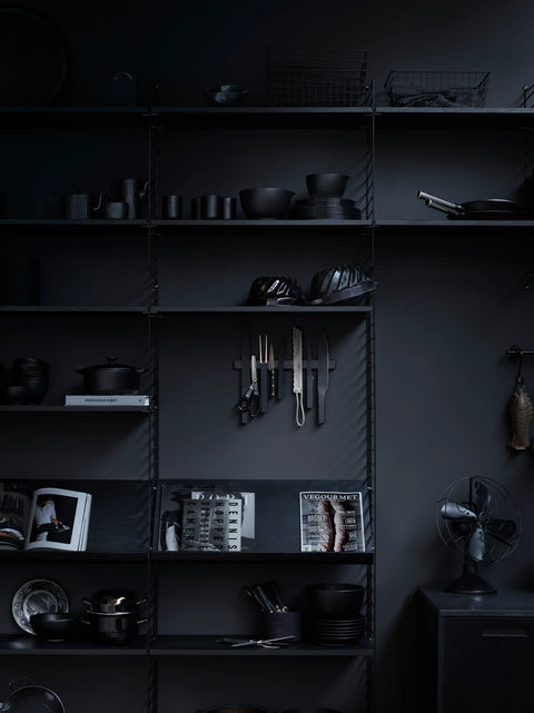 String Furniture black shelving system styled with kitchenware, books, and utensils in a dark interior