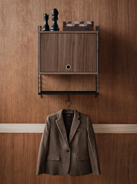 Brown blazer hanging on black String® System coat hanger beneath wall-mounted cabinet.