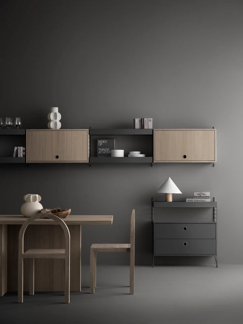 Scandinavian dining and living space featuring oak String® System cabinets with flip doors and black frame shelving