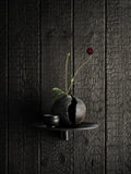 Museum NM&.045 shelf by String™ in black styled with cracked ceramic vase, small cup, and dark red flower on charred wood wall
