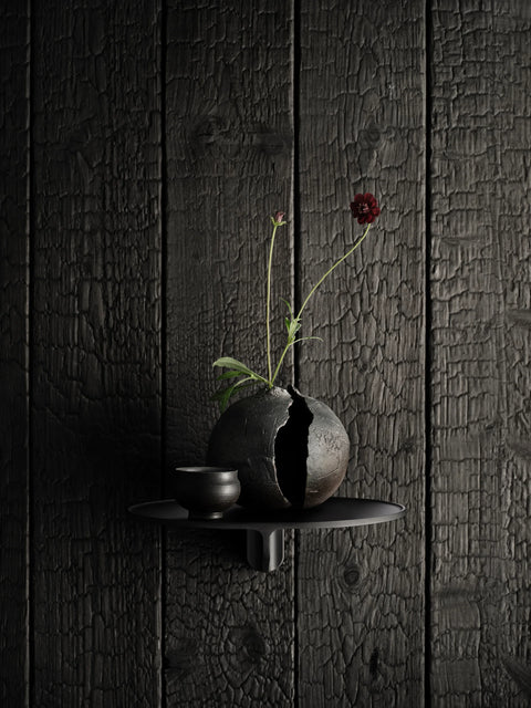 Museum NM&.045 shelf by String™ in black styled with cracked ceramic vase, small cup, and dark red flower on charred wood wall