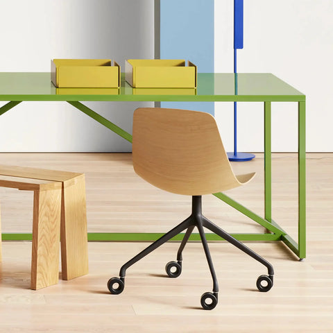 Blu Dot Clean Cut Task Chair in white oak veneer with black powder-coated aluminum five-star caster base, styled in a modern office beside a green steel desk with yellow storage bins and wood stool