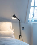 njp long arm wall lamp in black in a bedroom above nightstand by louis poulsen