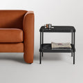 Blu Dot ComeHither Side Table in black marble styled beside a cognac leather sofa — two-tier design with marble top shelf holding a brass cup and lower shelf stacked with magazines