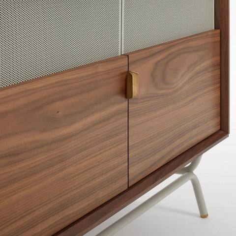 Blu Dot Dang Media Stand close-up detail in walnut veneer with grey perforated steel door front, antique brass pull, and putty powder-coated steel leg