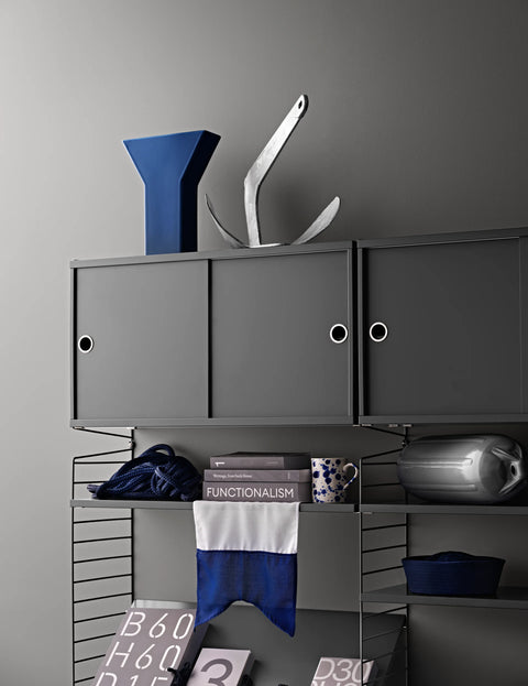 String Furniture cabinet with sliding doors in dark grey, styled with books and decor in a Scandinavian modular shelving system