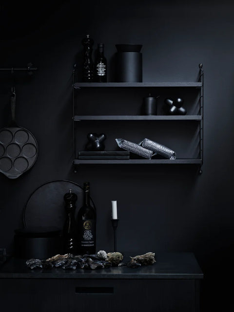 Black String® Pocket shelf in a moody kitchen setting with cookware, spices, and candles – Scandinavian wall shelving