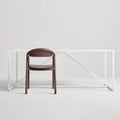Blu Dot Dibs Chair in oxblood stained beech wood, styled in front of a minimal white steel frame desk against a soft grey background
