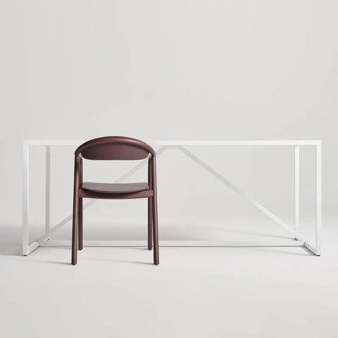Blu Dot Dibs Chair in oxblood stained beech wood, styled in front of a minimal white steel frame desk against a soft grey background
