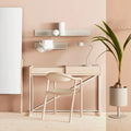 Blu Dot Dibs Chair in Day natural beech wood, styled in a modern home office beside a light wood desk with wall-mounted shelving, table lamp, and potted palm against a warm blush wall