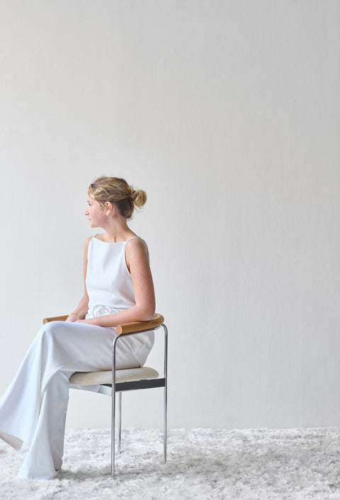 A woman seated on a DK3 Baia Chair in Balmoral White 02 with an oak back and chrome frame