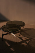 DK3 Baia Coffee and Side Table, two round graphite glass tables casting long shadows across a terrazzo floor