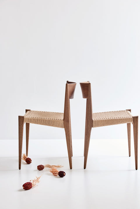 Two DK3 Pia Chairs in smoked oak, back to back, with dried flowers on the floor