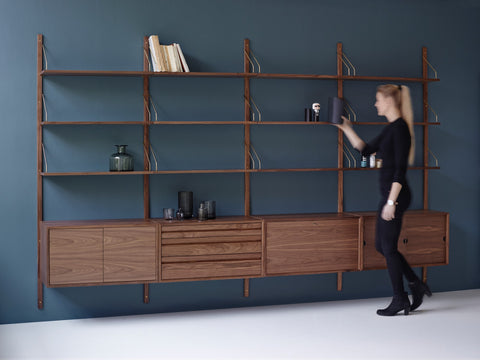 DK3 Royal System in walnut with brass hangers against a blue wall, a woman arranging the shelves