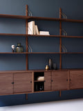 DK3 Royal System walnut shelves with brass hangers against a blue wall, close view