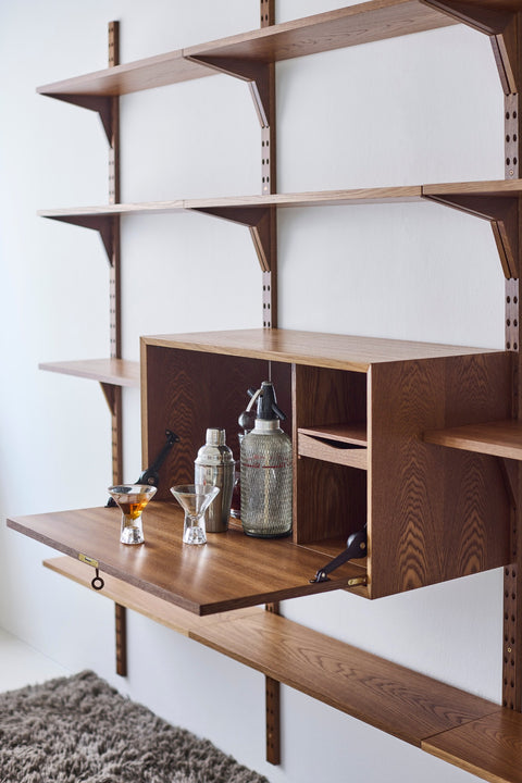 DK3 System Cado drop-front cabinet in smoked oak, open with a cocktail shaker and glasses