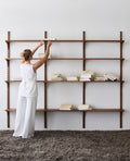 DK3 System Cado smoked oak shelving on wall rails, a woman reaching to the top shelf