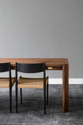DK3 Jeppe Utzon Table #1 in walnut, corner of the table with a black framed paper cord chair on a grey rug