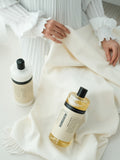 Humdakin 01 Fabric Softener, Chamomile & Sea Buckthorn, liquid fabric softener, softener and laundry soap bottles on a white knitted throw being folded by hand