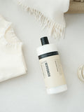 Humdakin 01 Fabric Softener, Chamomile & Sea Buckthorn, liquid fabric softener, bottle lying on a white knitted throw seen from above