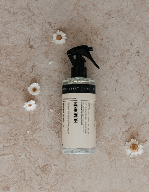 Humdakin Room Spray 2-in-1, Salvia & Sea Buckthorn, odour neutralising room spray, bottle on a stone surface with small daisies