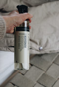 Humdakin Fabric Spray 2-in-1, Chamomile & Sea Buckthorn, textile refresher spray, held in a hand over rumpled beige bedding