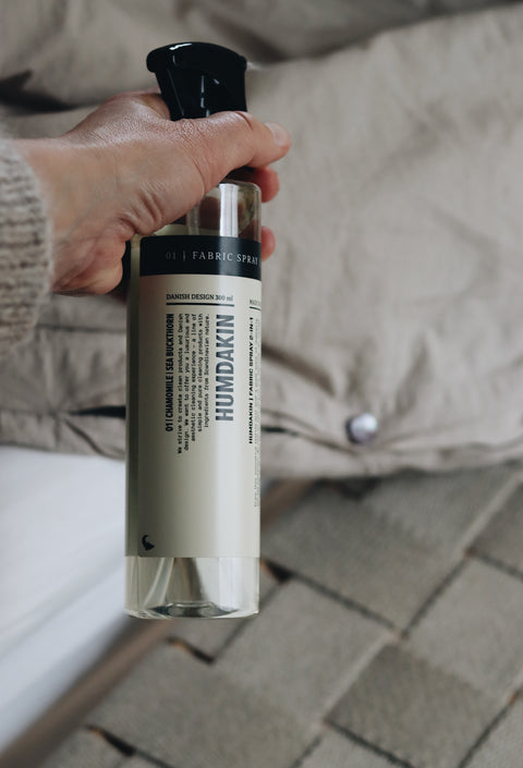 Humdakin Fabric Spray 2-in-1, Chamomile & Sea Buckthorn, textile refresher spray, held in a hand over rumpled beige bedding