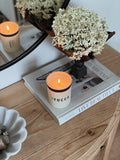 Humdakin Scented Candle, Yucca, scented candle in a glass, lit on a stack of books beside white hydrangeas on a wooden console
