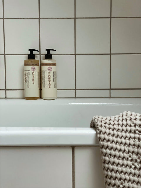 Humdakin 01 Conditioner, Chamomile & Sea Buckthorn, hair conditioner, bottles on the edge of a bathtub against white tiles with a knit towel