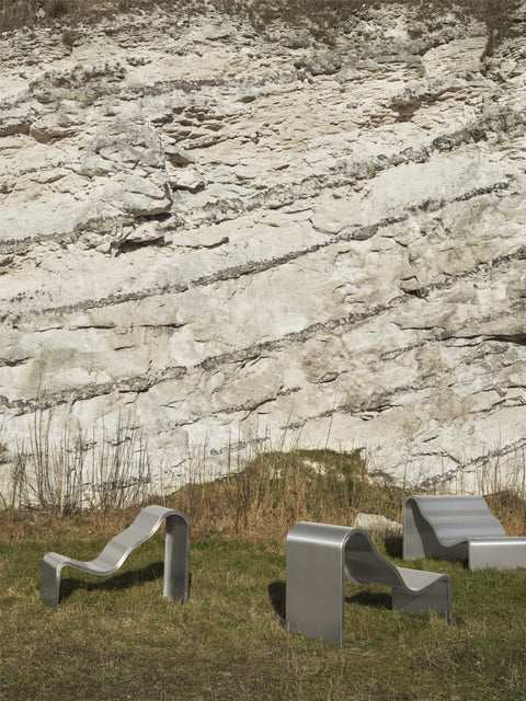 Muuto Dream View Benches in brushed steel placed outdoors against a natural rock wall backdrop
