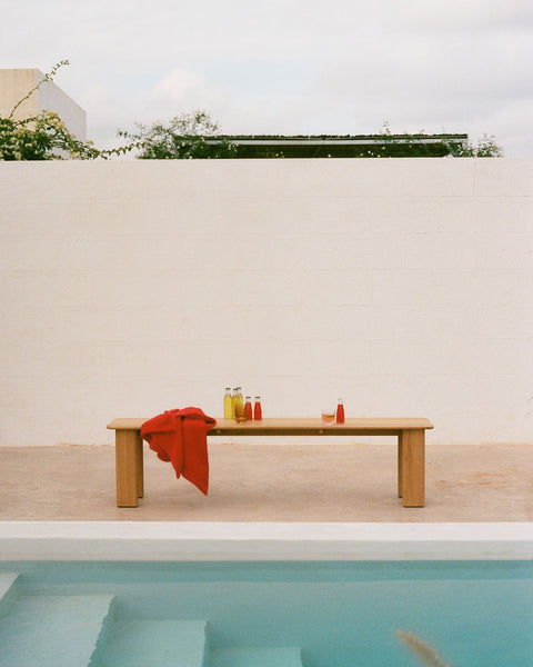 Muuto Assemble Bench in teak placed poolside with red throw and drinks on slatted seat