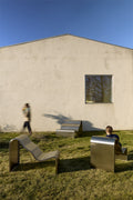 Group of Muuto Dream View Benches in brushed steel arranged on grass with people interacting
