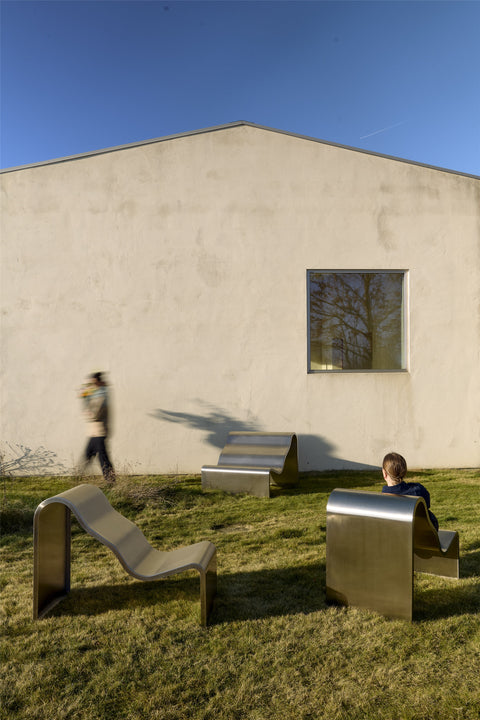 Group of Muuto Dream View Benches in brushed steel arranged on grass with people interacting