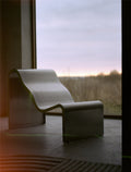 Muuto Dream View Bench in brushed steel positioned by a large window with sunset view