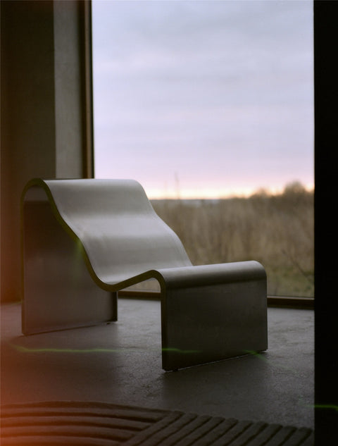 Muuto Dream View Bench in brushed steel positioned by a large window with sunset view