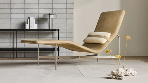 Blu Dot Deep Thoughts Leather Chaise in sand aniline leather with shearling lumbar pillow on stainless steel base, styled in a modern room with tile wall and dried yarrow