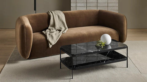 Blu Dot Comehither Coffee Table in black Marquina marble and matte black steel, styled in a modern living room with a camel velvet sofa, cream rug, and white sphere decor