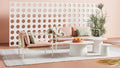 Blu Dot Dog Days Outdoor 2 Seat Sofa in Sunbrella Blush pink cushions with white powder-coated aluminum frame and all-weather rattan, styled with matching lounge chair and white side tables against a perforated breeze block wall